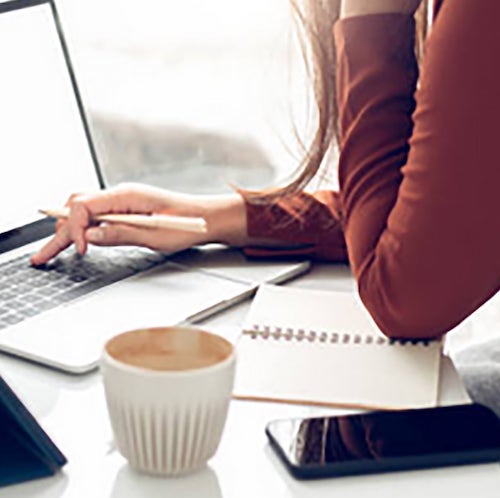 Woman searching for jobs on laptop with coffee and phone near her